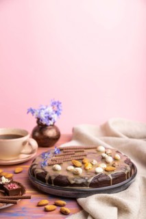 Homemade chocolate brownie cake with caramel cream and almonds with cup of coffee on a colored and