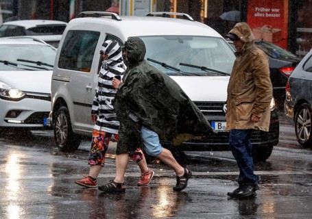 People in rain gear walking across a street in heavy rainfall, Berlin, 23 06 2023