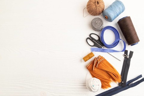 Sewing accessories: scissors, thread, thimbles, braid on white wooden background. Top view, flat