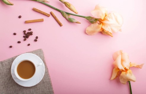 Orange iris flowers and a cup of coffee on pastel pink background. Morninig, spring, fashion