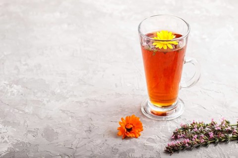 Glass of herbal tea with calendula and hyssop on a gray concrete background. Morninig, spring,