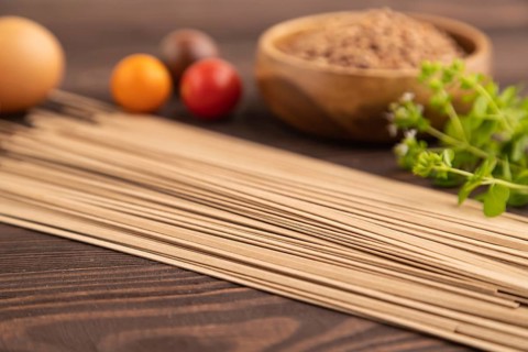 Japanese buckwheat soba noodles with tomato, eggs, spices, herbs on brown wooden background. Side