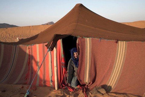 Model Released Young tourist boy dressed with blue nomad head scarf kneels at the entrance to a