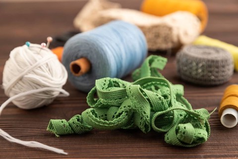 Sewing accessories: scissors, thread, thimbles, braid on brown wooden background. Side view, close