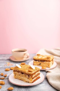 Honey cake with milk cream, caramel, almonds and a cup of coffee on a gray and pink background and