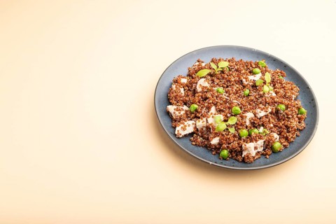 Quinoa porridge with green pea and chicken on ceramic plate on a pastel orange background. Side