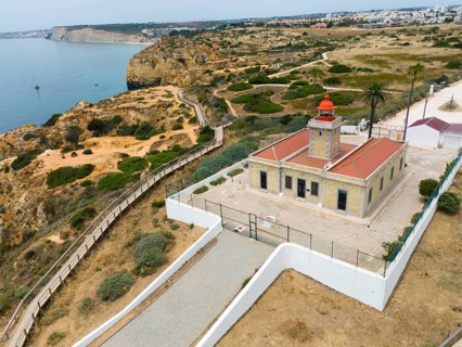 A lighthouse on the coast, surrounded by cliffs, the sea and town in the background. A path leads
