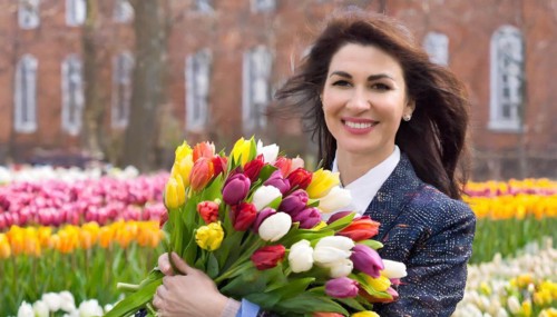 Smiling woman holding a colourful bouquet of tulips, in front of a historic brick house, AI
