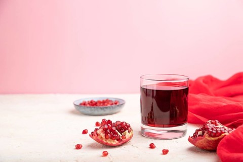 Glass of pomegranate juice on a white and pink background with red textile. Side view, copy space,