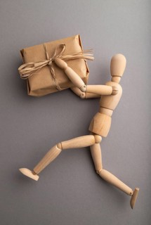 Wooden mannequin holding a gift box on gray pastel background. close up, isolated, delivery concept