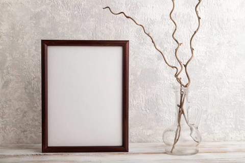 Brown wooden frame mockup with dried wine branch in glass on gray concrete background. Blank,