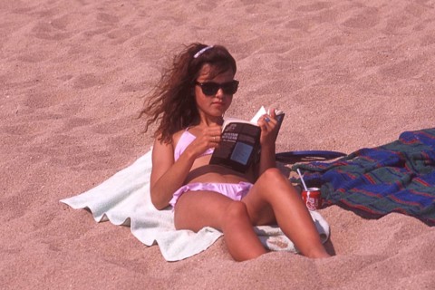 Young woman sunbathing on the beach and reading a book in Calella, Costa Brava, Barselona,