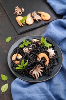Black cuttlefish ink pasta with shrimps or prawns and small octopuses on black concrete background