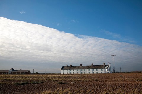 Frontal clouds passing over Coastguard Cottages shingle beach at Shingle Street, Suffolk, England,