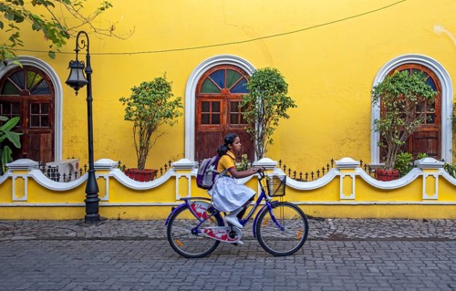 Street scene with girl on bicycle in front of yellow house, Fort Kochi, Cochin, Kerala, India, Asia
