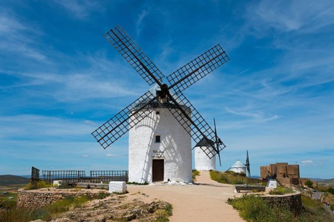 White windmill in front of a blue sky with few clouds, surrounded by nature and historical