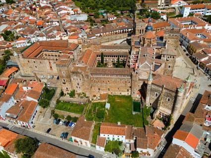 Aerial view of an old monastery with courtyard and red roofs, surrounded by a village in Spain.