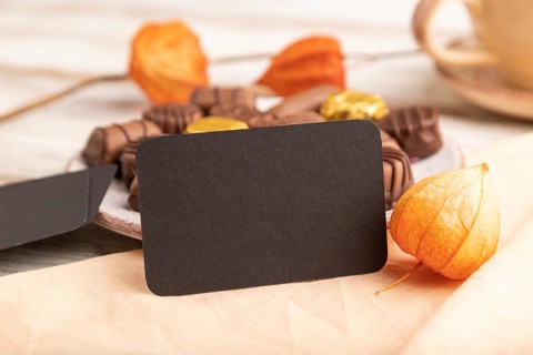 Black business card with chocolate candies and physalis flowers on a white wooden background and
