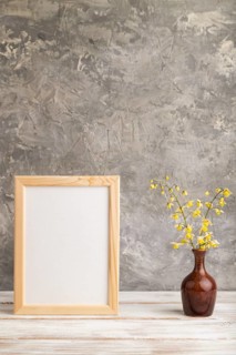 Wooden frame with yellow barrenwort flowers in ceramic vase on gray concrete background. side view,