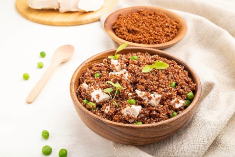 Quinoa porridge with green pea and chicken in wooden bowl on a white wooden background and linen