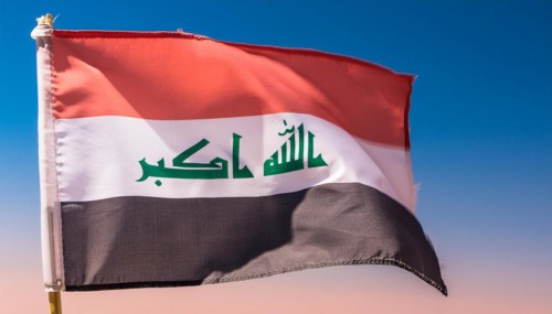 The flag of Iraq flutters in the wind, isolated against a blue sky
