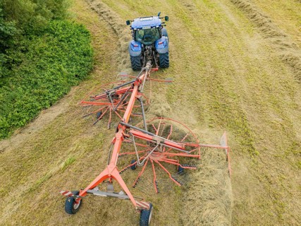 Aerial view of a tractor with hay machine in a field, surrounded by cut grass and hay bales,