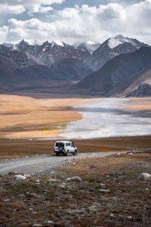 Off-road vehicle on a gravel track, glaciated and snow-covered peaks, Ak Shyrak Mountains, near