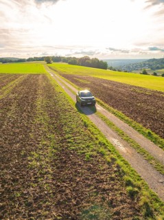 A car on a country road between wide fields under a sky with evening sunlight, car sharing, VW ID5,