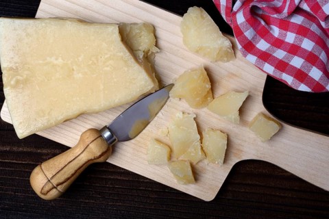 A piece of Parmesan cheese and chopped pieces of cheese on a wooden board