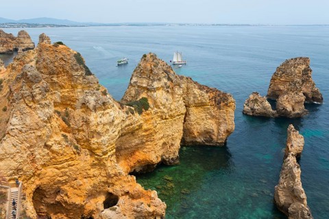 Rugged cliffs and rocks rise from the crystal clear water near sailing boats, Ponta da Piedade,