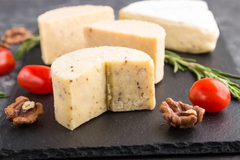 Cheddar cheese and various types of cheese with rosemary and tomatoes on black slate board on a