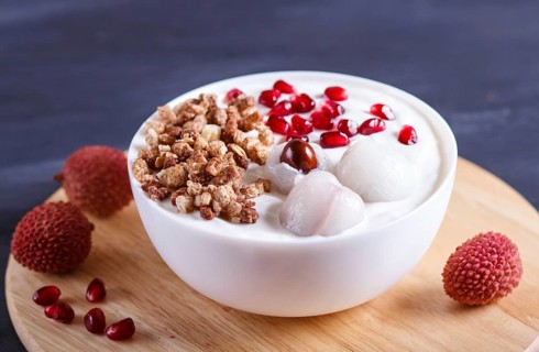 Greek yogurt with lychee, pomegranate seeds and granola in a white plate on a black wooden