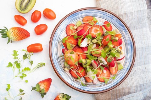 Vegetarian fruits and vegetables salad of strawberry, kiwi, tomatoes, microgreen sprouts on white