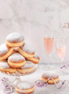 Doughnuts on a glass stand, rosé sparkling wine is poured in the background, falling icing sugar