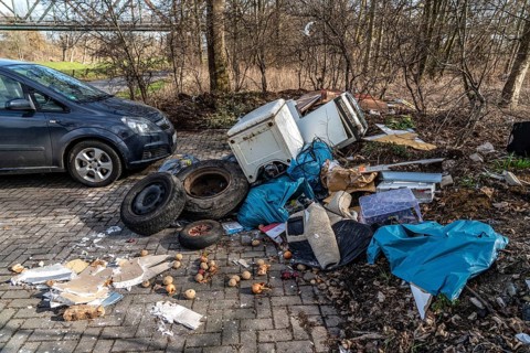Illegal waste disposal in a car park, in a wooded area, tyres, furniture, refrigerators, household