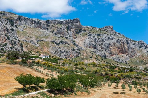 Barren rocky landscape with a small farmhouse surrounded by fields under a clear sky, nature