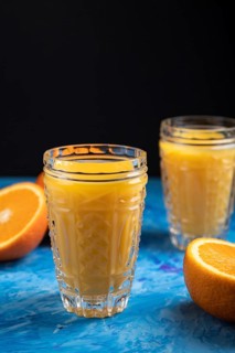 Glass of orange juice on a black and blue background. Hard light, contrast. Side view, close up