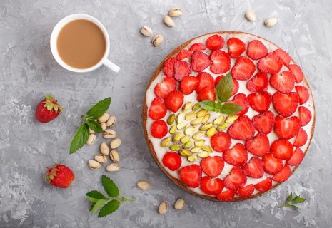 Homemade cake with yoghurt cream, strawberry, pistachio and a cup of coffee on a gray concrete