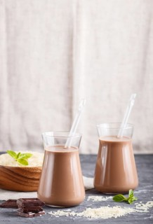 Organic non dairy rice chocolate milk in glass and wooden plate with rice seeds on a black concrete