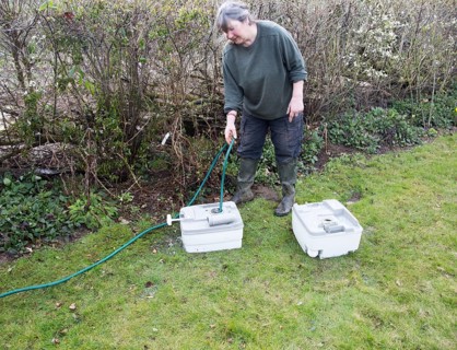 Woman using garden hose water pipe to wash clean camping toilet container cartridge, UK