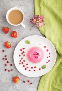 Pink mousse cake with strawberry and a cup of coffee on a gray concrete background and green