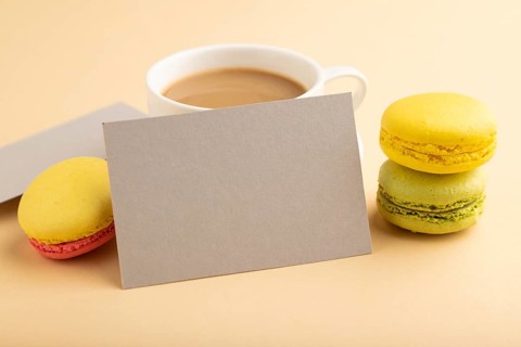 Gray paper business card mockup with yellow and green macaroons and cup of coffee on orange pastel