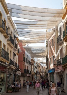 Fabric spread over buildings to provide shade in busy shopping street in central Seville, Spain,