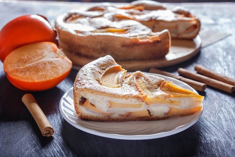 A slice of sweet persimmon pie on black wooden background. close up