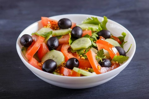Vegetarian salad of tomatoes, cucumbers, parsley, olives and mustard on black wooden background,