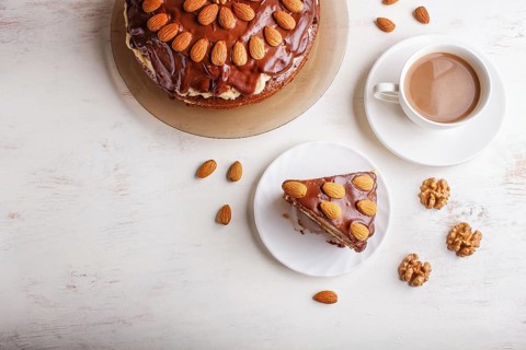 Homemade chocolate cake with milk cream, caramel and almonds on white wooden background. cup of