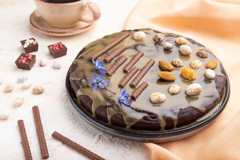 Homemade chocolate brownie cake with caramel cream and almonds with cup of coffee on a white
