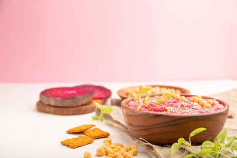 Hummus with beet and microgreen basil sprouts in wooden bowl on a white and pink background and