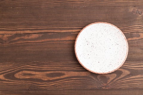 Empty white with dots ceramic plate on brown wooden background. Top view, copy space, flat lay
