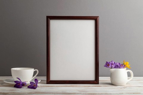 Brown wooden frame mockup with snowdrop crocus flowers and white coffee cup on gray paper